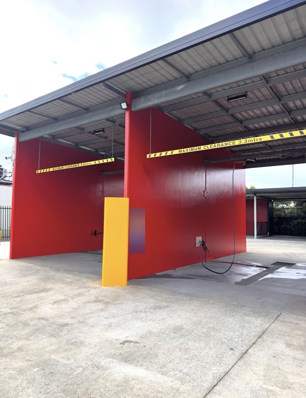 Freshly repainted red car wash bays with yellow safety bollard covers, commercial painting job in the Illawarra