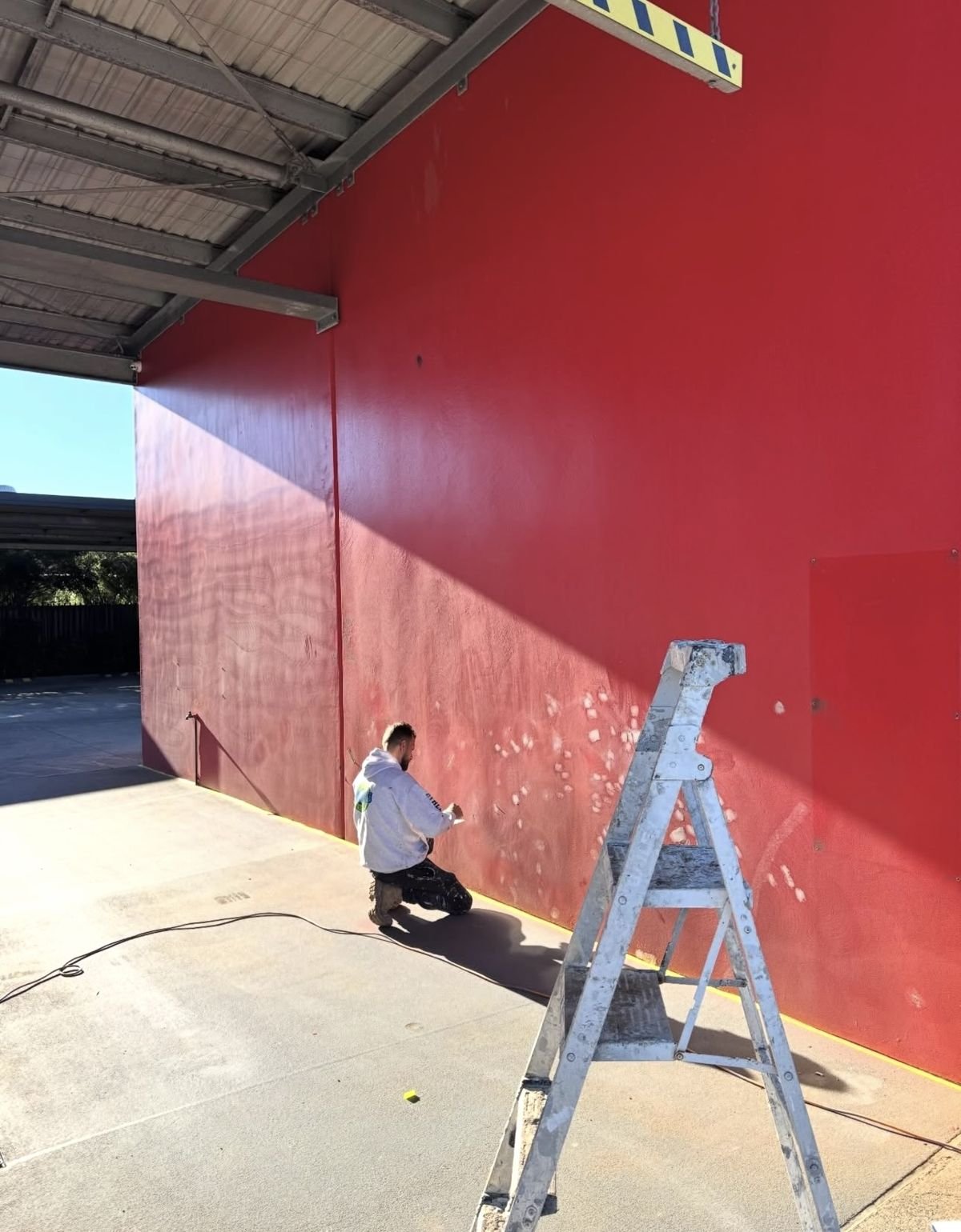 Colourland painter sanding and spot-priming a red car wash wall in Wollongong before repainting